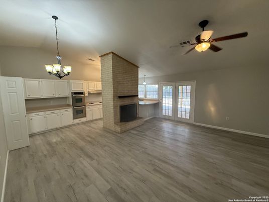 Chandelier, Empty room, Fireplace, Interior, Kitchen, Pendant Lights, Stainless Steel Appliances, Stone Walls, Wood Texture Flooring